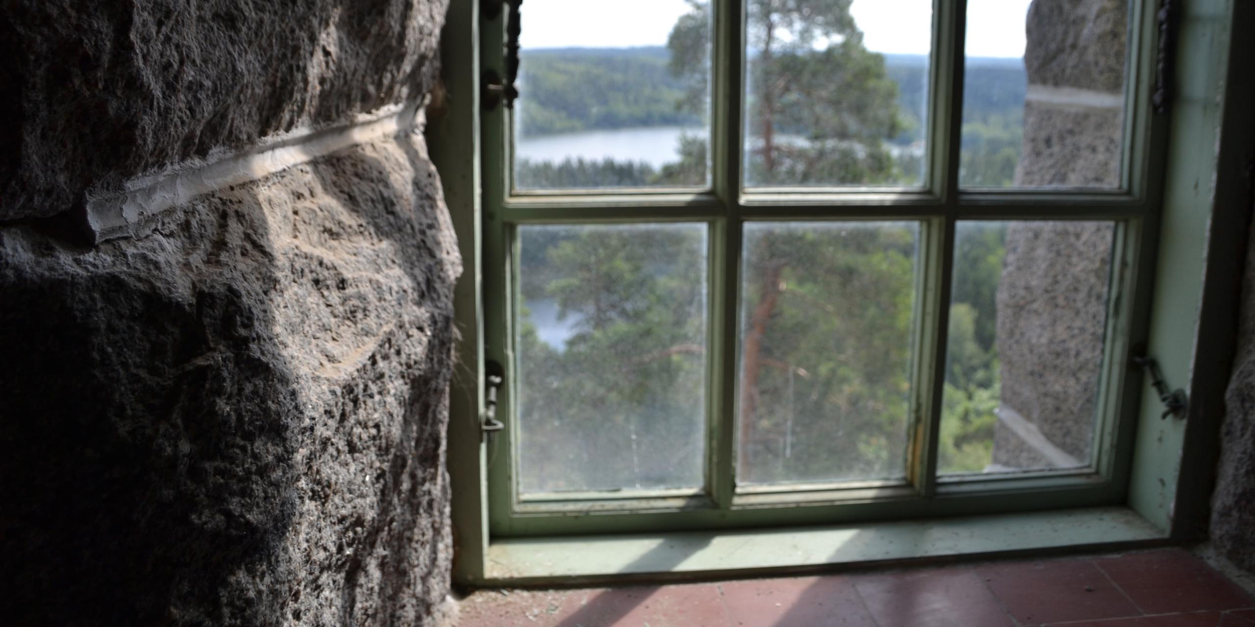 Näköala Aulangon näkötornin paksuihin harmaakivisiin seiniin upotetun vanhan ikkunan läpi kohti Aulangonjärven kansallismaisemaa.
